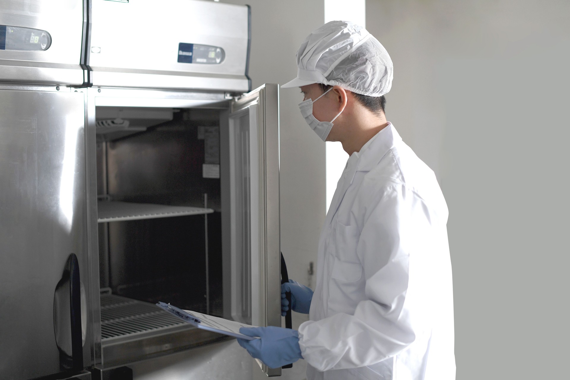 Un hombre asiático vestido con ropa sanitaria inspecciona un gran refrigerador en la cocina